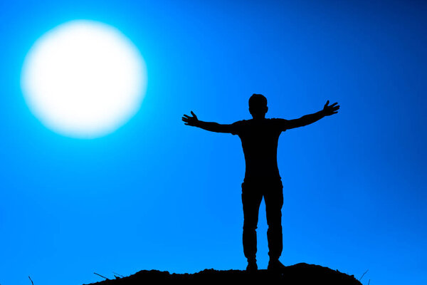 Silhouette of man raising his hands on the rock when sunse