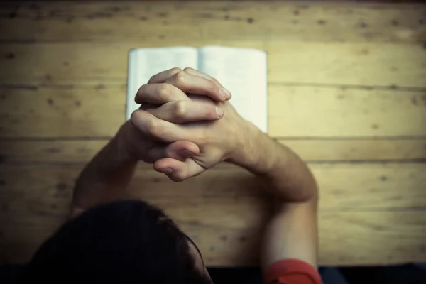 Praying hands with bible on the wooden desk background.