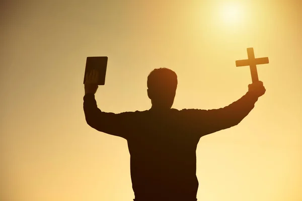 hands holding wooden cross and bible on sunrise backgroun