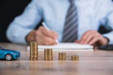 Adam elinde not defteri ve araba modeliyle para tutuyor.