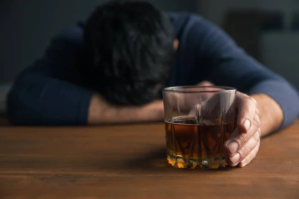 Üzgün adam masanın üstünde alkol bardağı var.