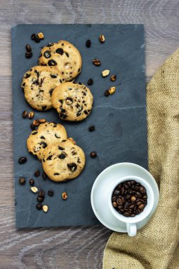 Bir çerez çikolata damla taş bir gemide kahve ve tahıl dağınık fıstık aittir. Yanında bir çuval bezi ve beyaz bir fincan kahve çekirdekleri ile