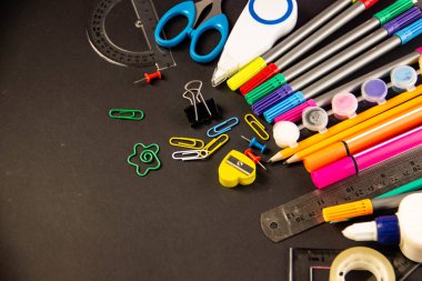 Keçe kalem, kalem, ataç, boya kalemi, cetveller, tutkal, düzeltmen, marker, makas, defter kalemtıraş alanı metin altında siyah bir zemin üzerine