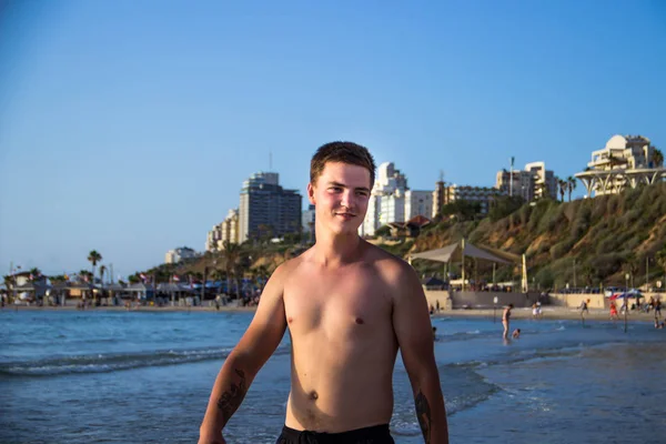 A young European man strolls by the sea and watches him