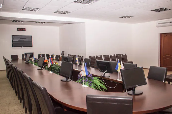 Oval table made of natural wood with leather seats in the conference hall with flags of Ukraine on it