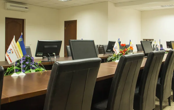 Oval table made of natural wood with leather seats in the conference hall with flags of Ukraine on it