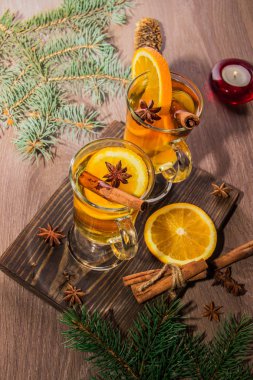 İki bardak portakal ve bir mum ve tinsel bir Noel ağacının dalları ile ahşap bir gemide baharat ile mulled şarap lezzetli kokulu çay ile.