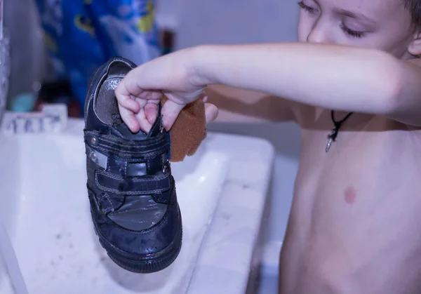 Childrens hands wash dirty sneakers in a white sink