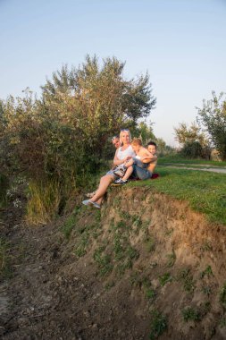 İki oğlu ile mutlu güzel aile günbatımında göl yakınındaki niteliğine oturuyor