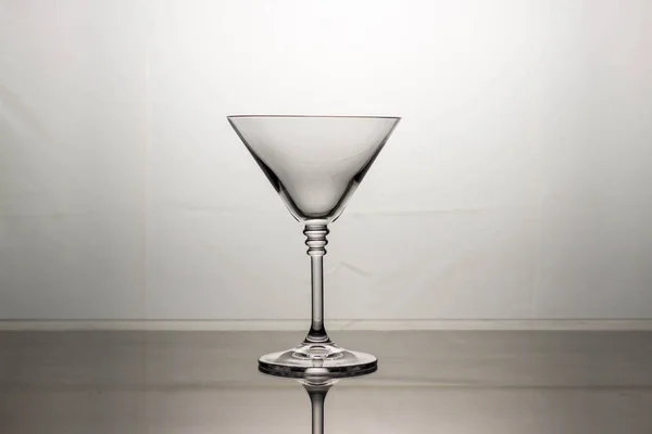 Empty cocktail glass on a mirrored table and light background