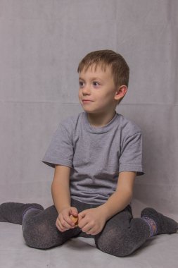Mutlu çocuk gri tişört içinde oturan ve hafif bir arka plan üzerinde gülümseyen