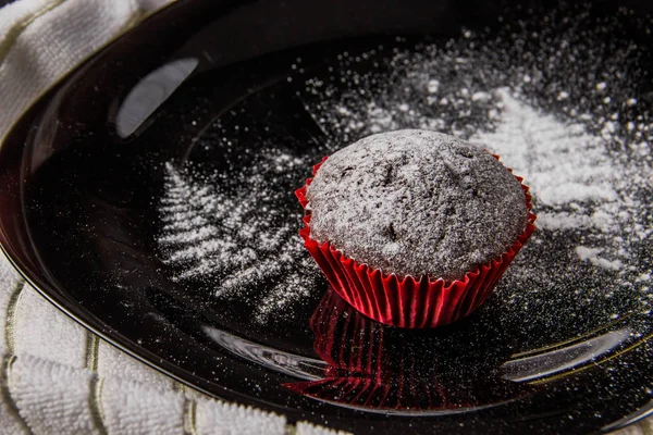 Muffins de chocolate em um fundo escuro com uma decoração de galho pintado com açúcar de confeiteiro — Fotografia de Stock