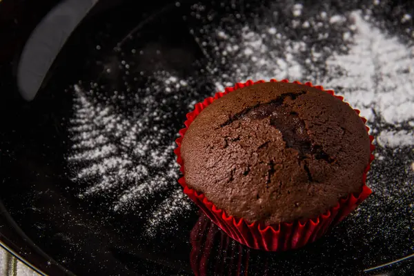 Muffins de chocolate em um fundo escuro com uma decoração de galho pintado com açúcar de confeiteiro — Fotografia de Stock