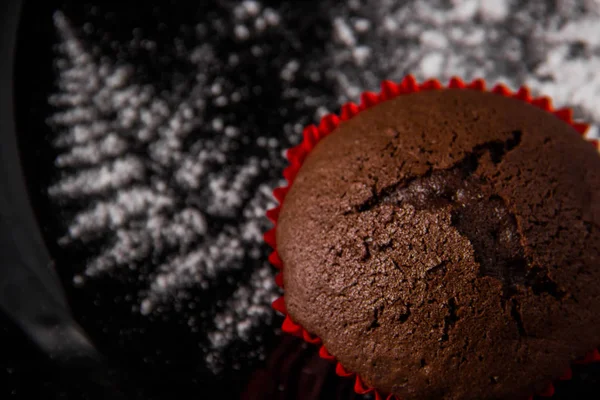 Muffins de chocolate em um fundo escuro com uma decoração de galho pintado com açúcar de confeiteiro — Fotografia de Stock