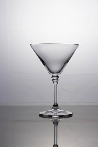 Empty cocktail glass on a mirrored table and light background