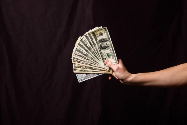 Hands holding a fan of dollars on a black background