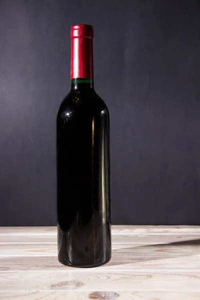 Μπουκάλι κρασί στέκεται πάνω σε ένα ξύλινο τραπέζι με ένα σκούρο φόντο. — Φωτογραφία Αρχείου