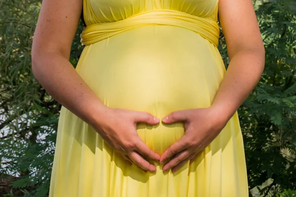 Belly of a pregnant happy woman in a yellow dress on the background of nature — Stock Photo, Image