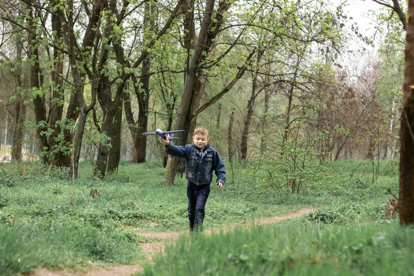 De jongen lanceert een blauw vliegtuig in de lucht in een dicht bos — Stockfoto