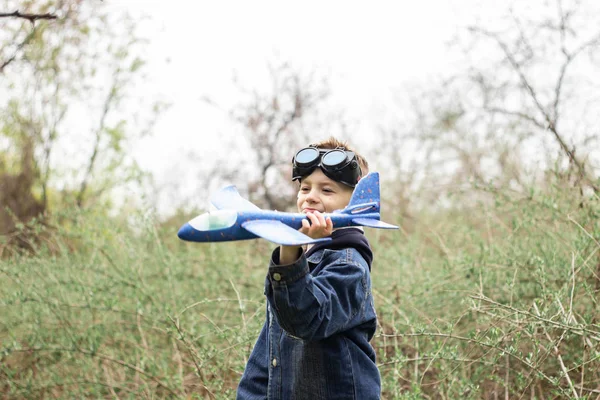 De jongen lanceert een blauw vliegtuig in de lucht in een dicht bos — Stockfoto