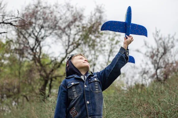El niño lanza un avión azul al cielo en un denso bosque — Foto de Stock