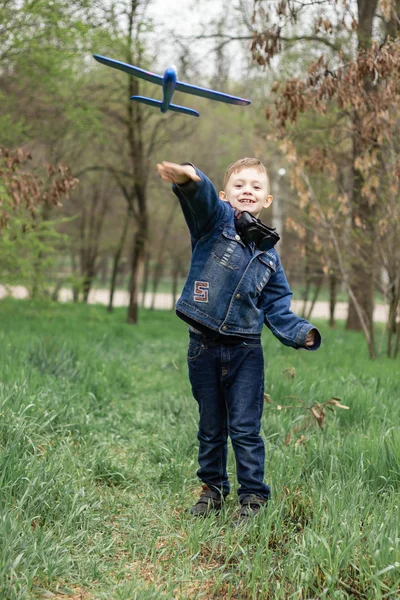 Мальчик запускает голубой самолет в небо в густом лесу — стоковое фото