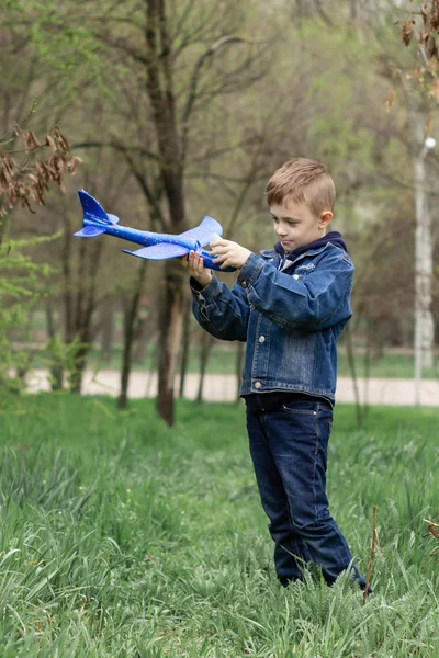 De jongen lanceert een blauw vliegtuig in de lucht in een dicht bos — Stockfoto