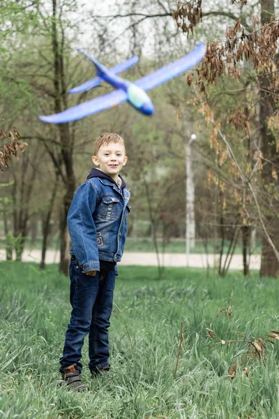 De jongen lanceert een blauw vliegtuig in de lucht in een dicht bos — Stockfoto