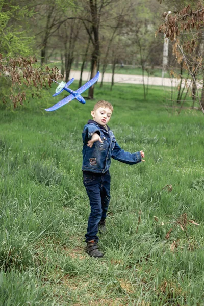 O menino lança um avião azul no céu em uma floresta densa — Fotografia de Stock