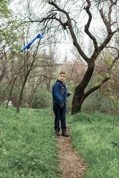 O menino lança um avião azul no céu em uma floresta densa — Fotografia de Stock