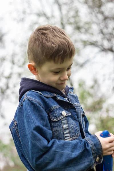 De jongen lanceert een blauw vliegtuig in de lucht in een dicht bos — Stockfoto