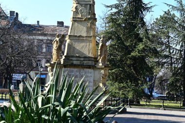 Şehir parkında yeşil bitki ve ağaçlarla çevrili bir anıt. 