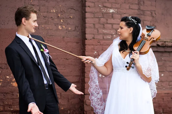 Bride joking with the groom playing the violin Stock Photo