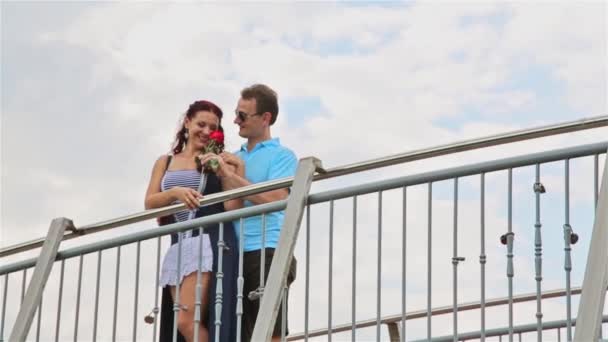 El hombre en el puente sorprendió a la hermosa chica, dándole una flor, una rosa roja — Vídeos de Stock