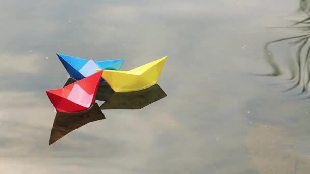 Три маленьких цветных бумажных лодки, плавающие по воде — стоковое видео