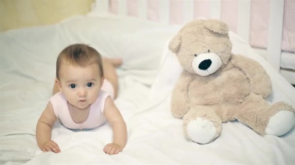 En liten flicka liggande bredvid en björn på en vit filt — Stockvideo