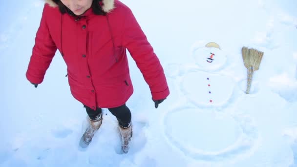 Chica bromeando cayó en la nieve al lado de un muñeco de nieve HD — Vídeos de Stock