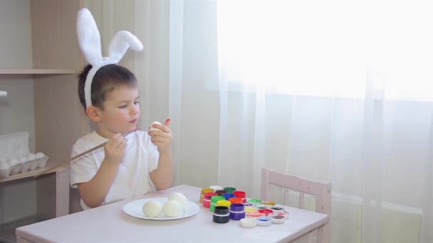 Um menino vestido de lebre pinta um ovo de Páscoa — Vídeo de Stock