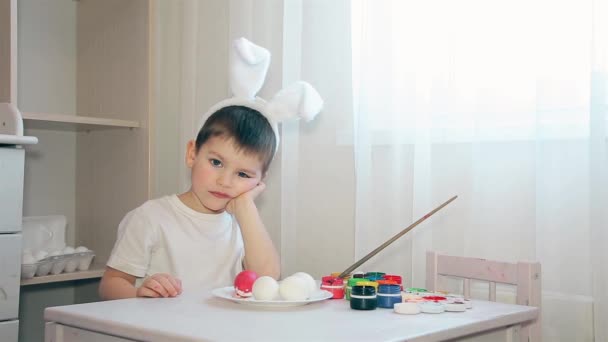 Un ragazzo vestito da lepre non sa di che colore decorare il colore dell'uovo di Pasqua. — Video Stock