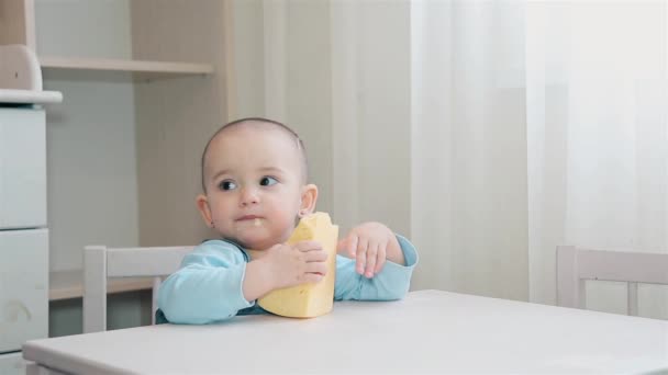 Un niño hambriento está sentado en un escritorio blanco en la casa de los niños y comiendo queso casero — Vídeo de stock