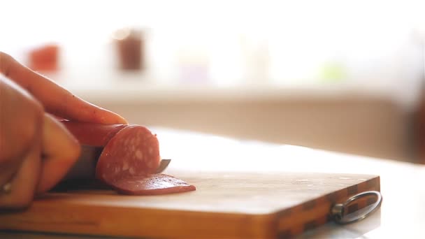 Uma mulher na aldeia corta pequenas fatias de salsicha em uma cozinha de madeira Board close-up — Vídeo de Stock