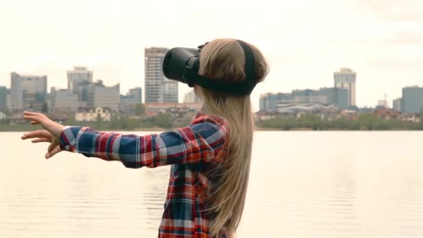 Ξανθιά κορίτσι με μακριά μαλλιά και γυαλιά VR στέκεται κοντά στη μεγάλη πόλη κοντά στη θάλασσα HD 1080 — Αρχείο Βίντεο