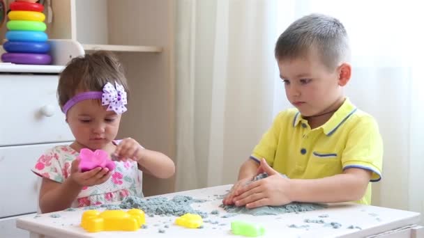 Мальчик и девочка в детском саду сидят за белым столом и играют с кинетическим песком — стоковое видео