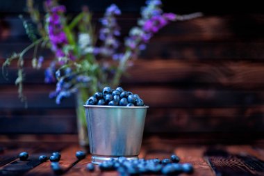 koyu ahşap arka plan BCC çiçek üzerine bir kova içinde yaban mersini. rustik tarzı