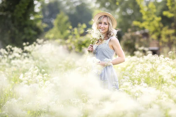 女性肖像户外 一个戴着草帽的女人 在花丛中 带着一束野花 该国的夏天 — 图库照片