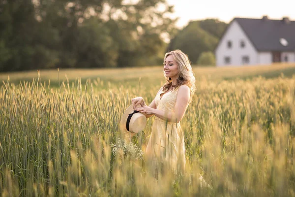 Solnedgång på sommaren. Landsbygdslivet. En ung kvinna på fältet kastar en hatt. Rustik stil — Stockfoto