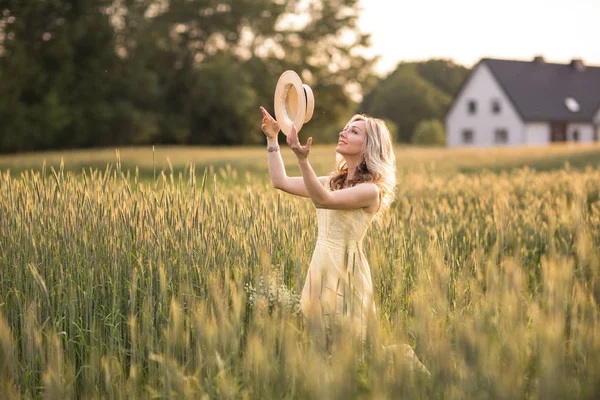 Solnedgång på sommaren. Landsbygdslivet. En ung kvinna på fältet kastar en hatt. Rustik stil — Stockfoto