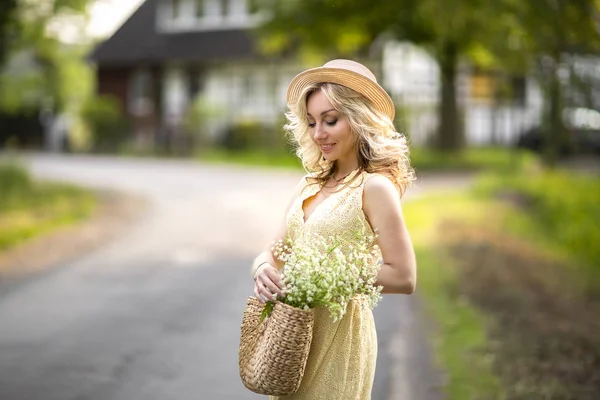 女性肖像户外。一个戴着草帽的女人，在花丛中，带着一束野花。该国的夏天 — 图库照片