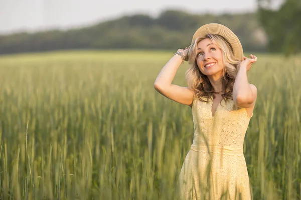 Landsbygdslivet. Vandra genom ängen blond ung kvinna i en hatt. Sommaren. — Stockfoto