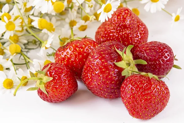 Scattered strawberries on a light background with a bouquet of chamomile flowers . Summer berry season. — Stock Photo, Image